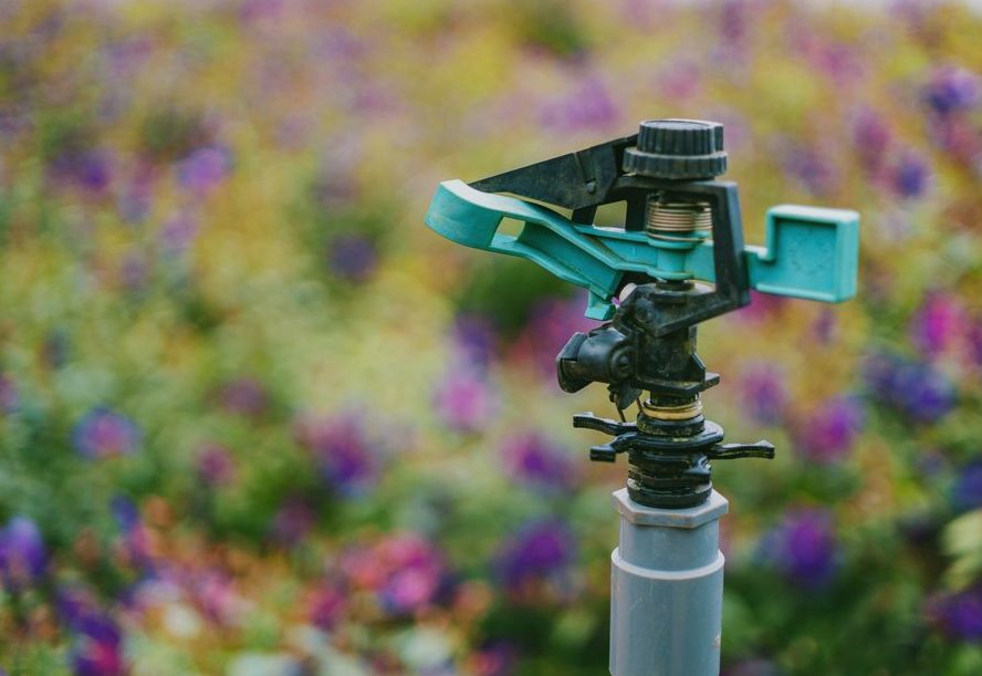 Detailed close-up of a garden sprinkler with colorful flowers in soft focus background