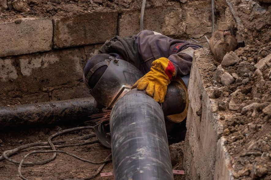 A worker welds a pipe in an urban trench, showcasing industrial construction work